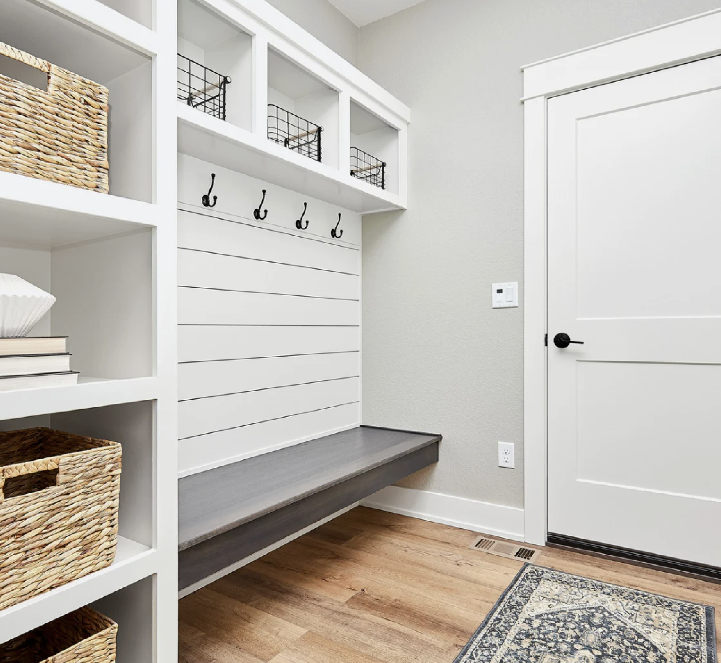 White shiplap mudroom with a bench, decorative rug, and woven baskets